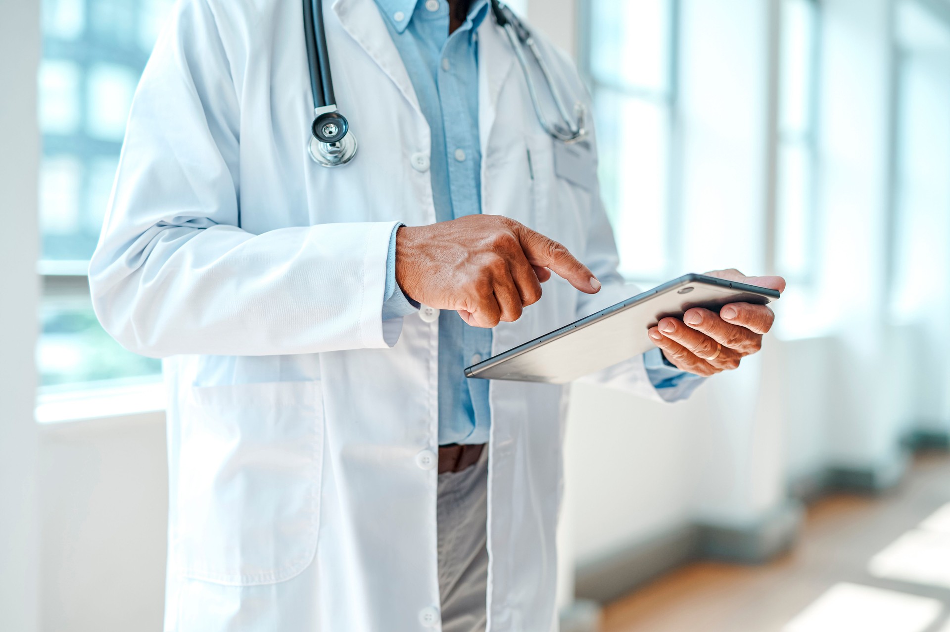 Male physician holding digital tablet, pointing at device in hospital lounge